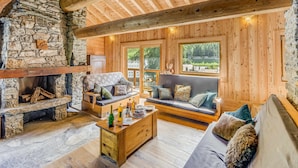 A cozy log cabin interior with a stone fireplace, wooden furniture, and large windows offering views of the outdoors. - Rustic chalet for 12, 5 rooms, Wifi in Tignes (Tignes-Les Brévières)