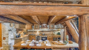 A rustic kitchen with wooden beams, stone walls, and a wooden dining table set for a meal. - Rustic chalet for 12, 5 rooms, Wifi in Tignes (Tignes-Les Brévières)