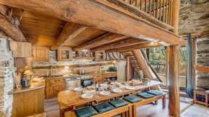 A rustic wooden kitchen with a long dining table set for four, benches with cushions, and a stone wall backdrop. - Rustic chalet for 12, 5 rooms, Wifi in Tignes (Tignes-Les Brévières)