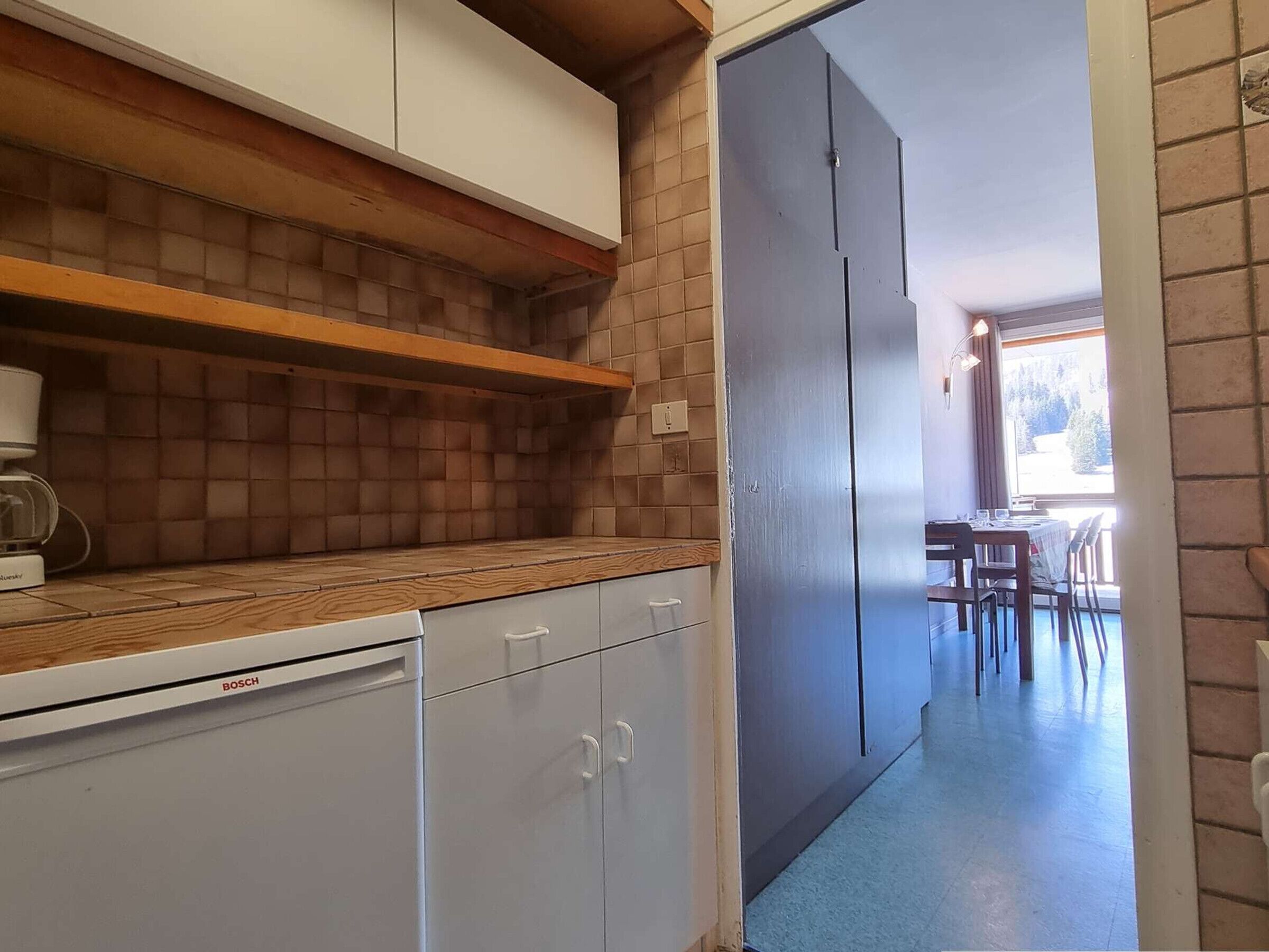 A kitchen with a Bosch dishwasher, wooden shelves, and a grey refrigerator.