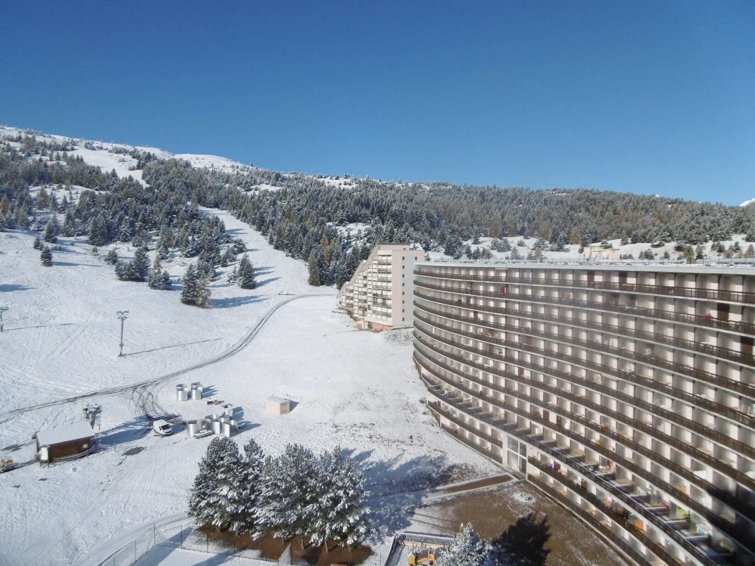 Un grand hôtel à plusieurs étages, entouré d’arbres couverts de neige et situé à proximité d’une piste de ski.