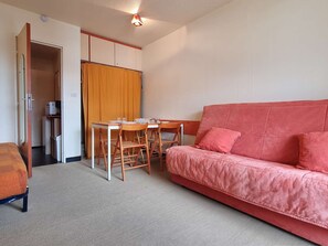 Une chambre d’hôtel compacte avec un canapé rouge, une petite table à manger avec des chaises, un coin cuisine et une salle de bain avec un rideau de douche.