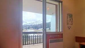 A room with a sliding glass door leading to a balcony with a view of snow-covered mountains and a wooden fence. - Cozy Studio for 3 with Free WiFi, Close to Slopes & Shops, Private Ski Locker, Parking Available (Le Dévoluy)