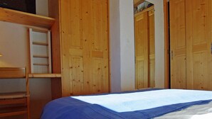 A bedroom with a bunk bed, wooden wardrobe, and a ladder.