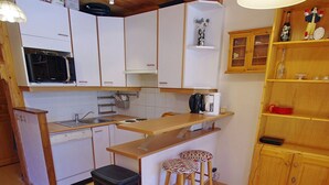 A compact kitchen with white cabinets, a microwave, a coffee maker, and a small wooden shelf with decorative items.