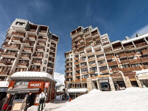 A high-rise hotel with multiple balconies, ski shops, and a snow-covered ground.
