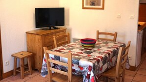 Ein kleiner Essbereich mit einem Tisch, der mit einer Patchworkdecke bedeckt ist, einem Fernseher auf einem Holzschrank und einem kleinen Hocker.