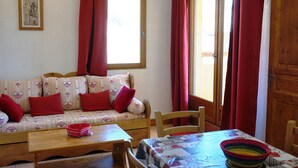 Ein gemütliches Zimmer mit einer Couch, einem Holztisch und einem Fenster mit roten Vorhängen.