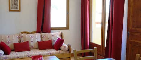 A cozy room with a sofa, a wooden table, and a window with red curtains.