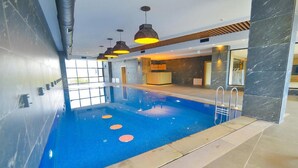 An indoor swimming pool with a blue tiled floor, a reception desk, and modern pendant lighting. - Serenity Comfort Hotel  (Istanbul)