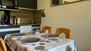 Un comedor con una mesa preparada para cuatro personas, una cocina con armarios oscuros y un espejo en la pared.