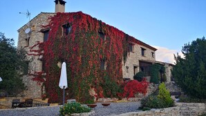 A stone building with red ivy covering the walls, a white umbrella, and outdoor seating. - More from lárlequí - Entire farmhouse (Rojals)