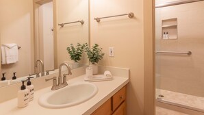 A bathroom with a sink, mirror, towel rack, and a shower area.