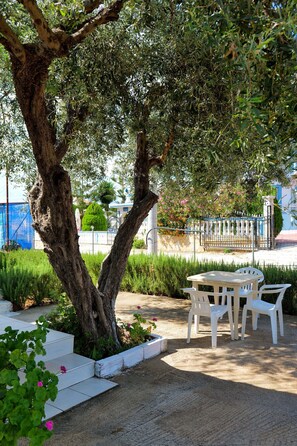 An outdoor seating area with a table and chairs, surrounded by greenery and a tree. - Vila Chris (Ksamil)