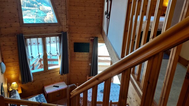 A wooden interior with a staircase, a bed, a table, and a TV.
