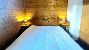 A room with wooden panel walls, a bed with white bedding, two bedside lamps, and a small decorative plant on the wall.