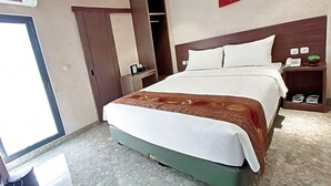 A hotel room with a bed, a wardrobe, a bedside table with a phone and a plant, and a door. - Lun Hotel Manado (Manado)