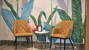 Two tufted chairs with black legs and a small round table with a potted plant and a framed picture. - Lun Hotel Manado (Manado)