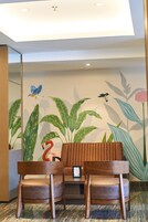 A reception area with two wooden chairs, a wall mural of birds and plants, and a ceiling light fixture.