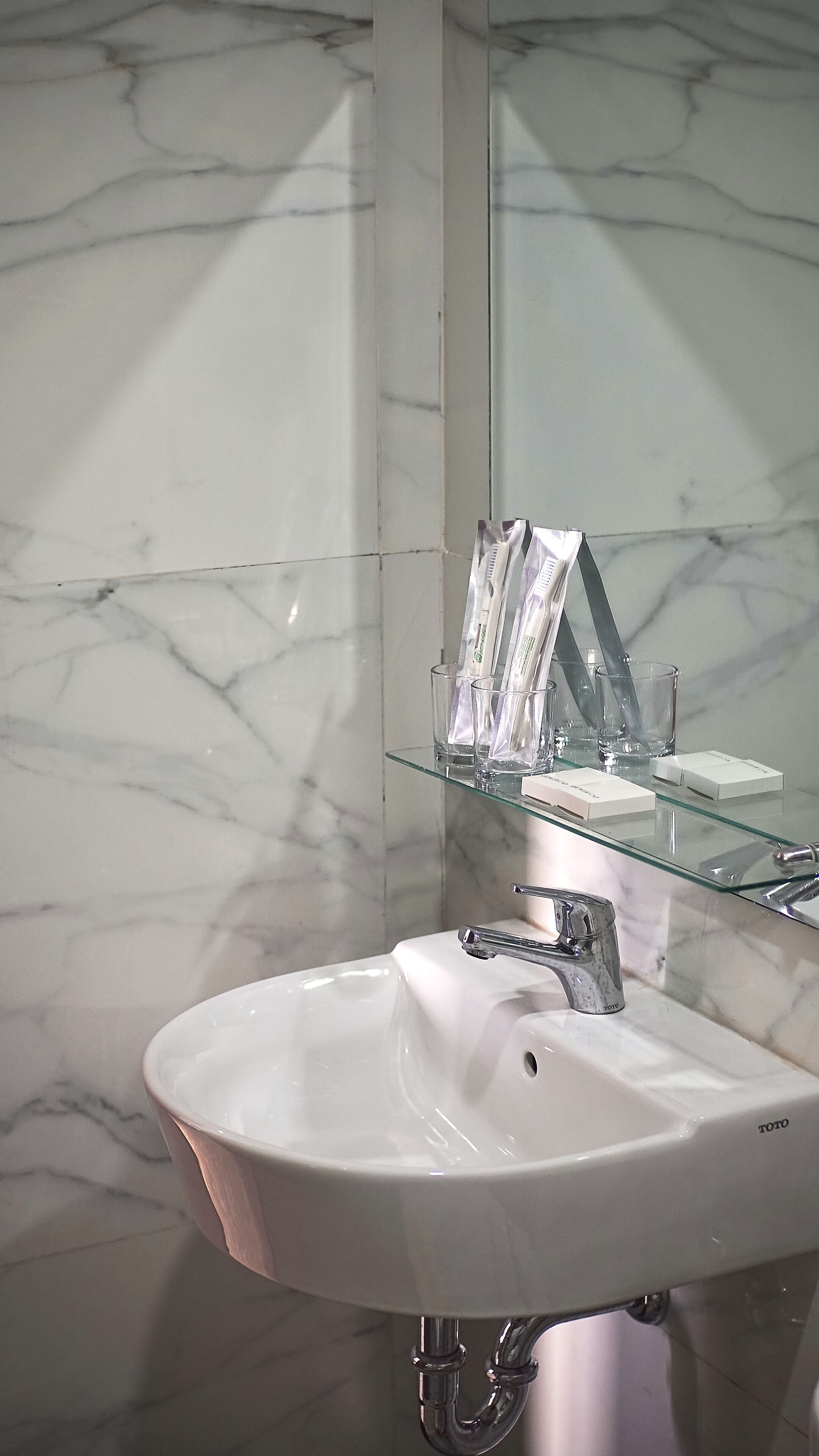 A bathroom with a white sink, a glass shelf with toiletries, and a mirror.