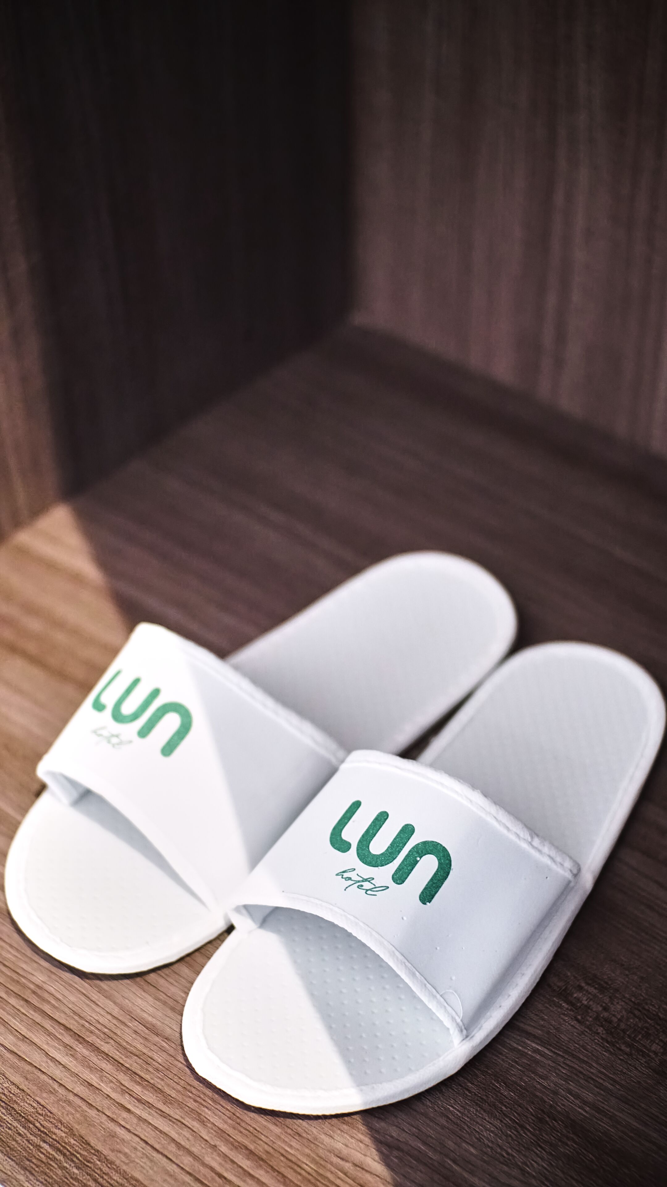 Ein Paar weiße Flip-Flops mit dem Aufdruck "lun hotel" auf einer Holzfläche.