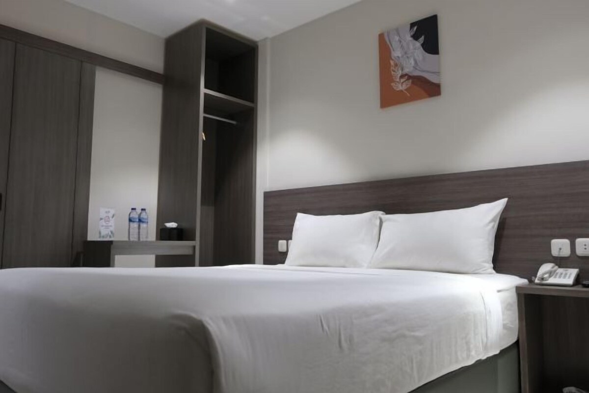 Une chambre d’hôtel avec un grand lit, une tête de lit en bois, une table de chevet avec un téléphone et un tableau au mur.