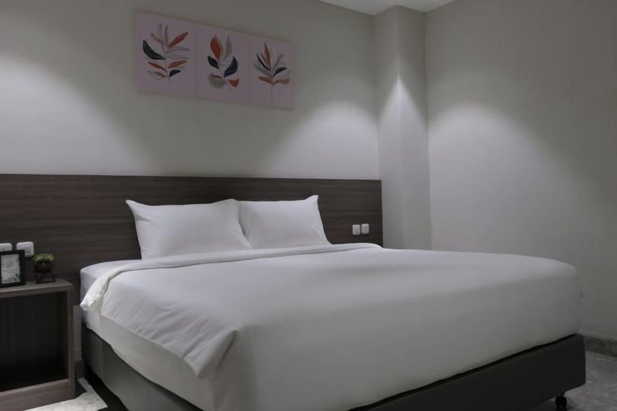 Une chambre à coucher moderne avec un grand lit, une tête de lit sombre et une table de chevet avec une lampe.