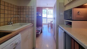 A compact kitchen with a sink, Bosch dishwasher, and a microwave. A wooden cabinet and a small dining area with a table and chairs are visible. - Cozy studio with WIFI 50m from slopes - 4 ppl (Le Dévoluy)