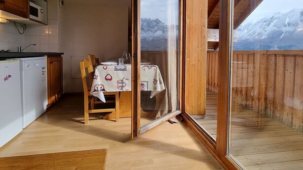 A kitchen with wooden cabinets and a dining area with a table set for two. - 2-room apartment with cabin - 6 ppl - Near slopes (Le Dévoluy)