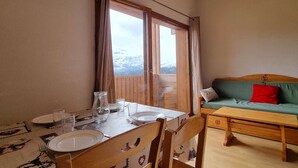 A dining area with a table set for two, a wooden bench with cushions, and a view of a snowy landscape through a large window. - 2-room apartment with cabin - 6 ppl - Near slopes (Le Dévoluy)