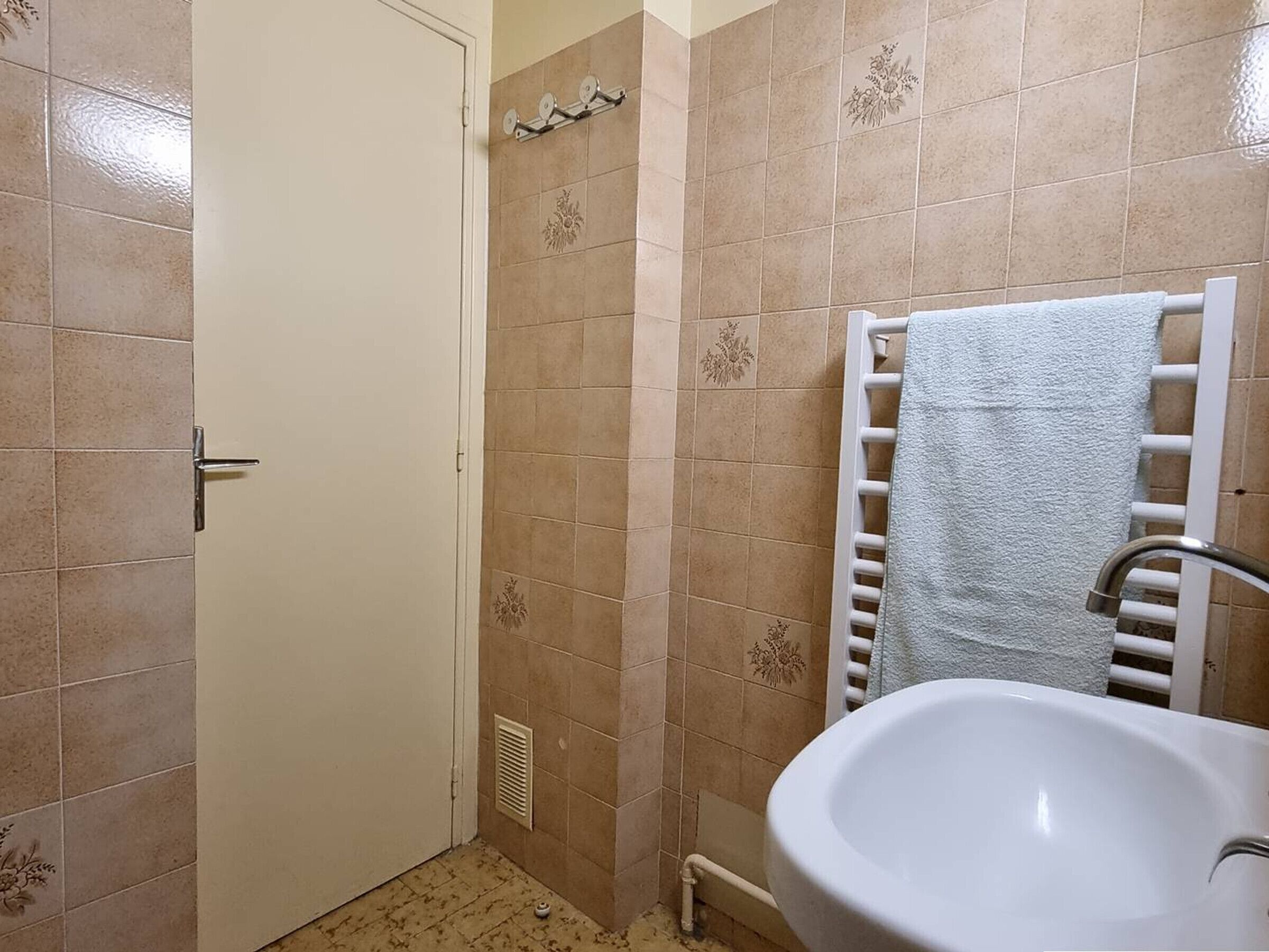 A bathroom with beige tiles, a white sink, a towel rack, and a door.