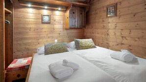 Habitación de cabaña de madera con dos camas, una ventana pequeña y techo de madera.