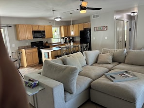 A modern kitchen with wooden cabinets, a black refrigerator, and a dining area with a gray sofa.