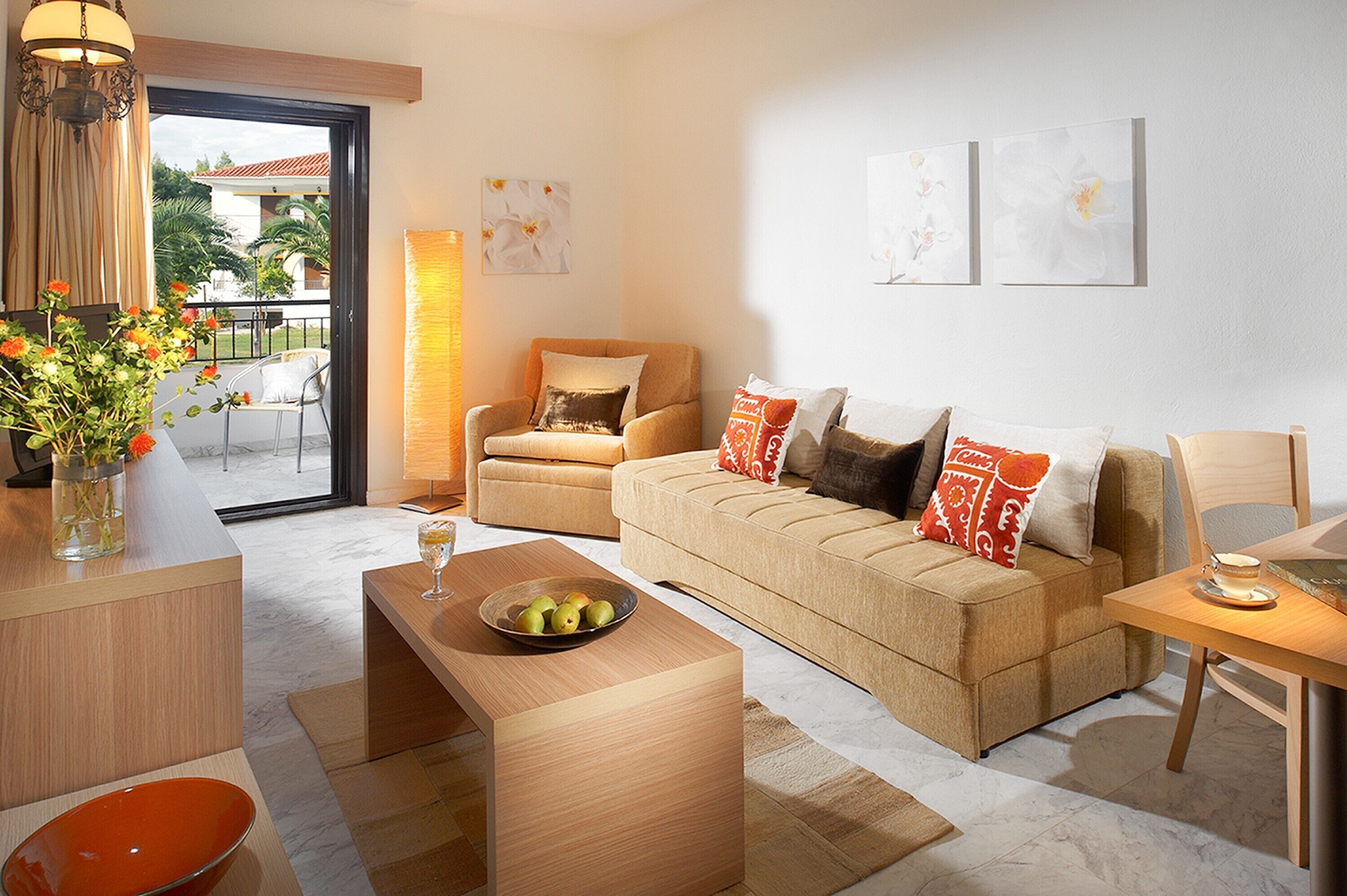 Una sala moderna con sofá, una mesa de centro con frutas, una mesa de comedor con una taza y vistas al exterior a través de una puerta de vidrio.