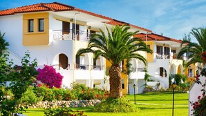 Un hotel de varios pisos con balcones, un jardín bien cuidado y un cielo azul despejado.