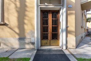 Ein Gebäudeeingang mit einer zweiflügeligen Holztür, einem Schild mit der Nummer 13 und einer schwarzen Fußmatte.