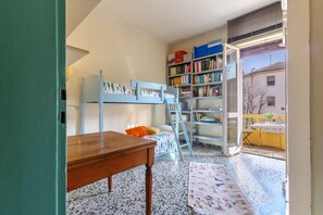 Een kamer met een stapelbed, een houten tafel, een boekenplank en uitzicht op buiten.