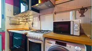 Une cuisine compacte équipée d’une cuisinière à gaz, d’un four à micro-ondes et d’un lave-linge.