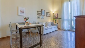 Un coin repas comprenant une table, des chaises et un canapé. Des tableaux encadrés ornent le mur et une lampe est posée sur la table.