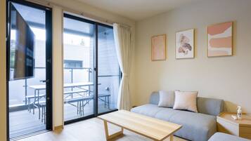 A modern hotel room with a sliding glass door to an outdoor patio, a sofa, a bedside table, and a small bedside table with a bottle.