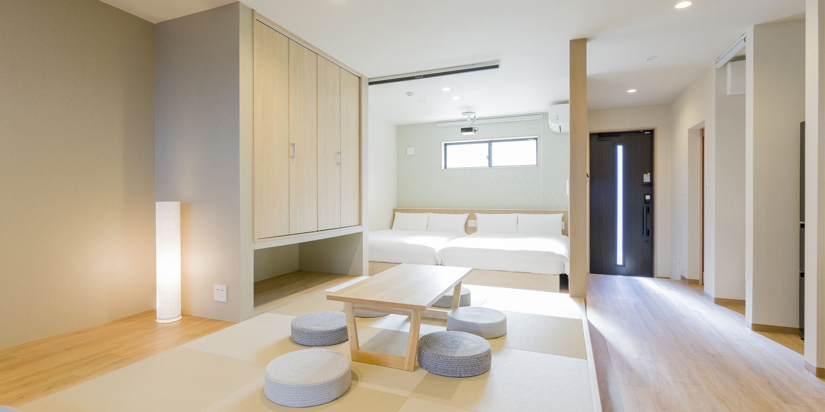A modern hotel room with a large wardrobe, a bed with white bedding, a small table, and a seating area with cushions.
