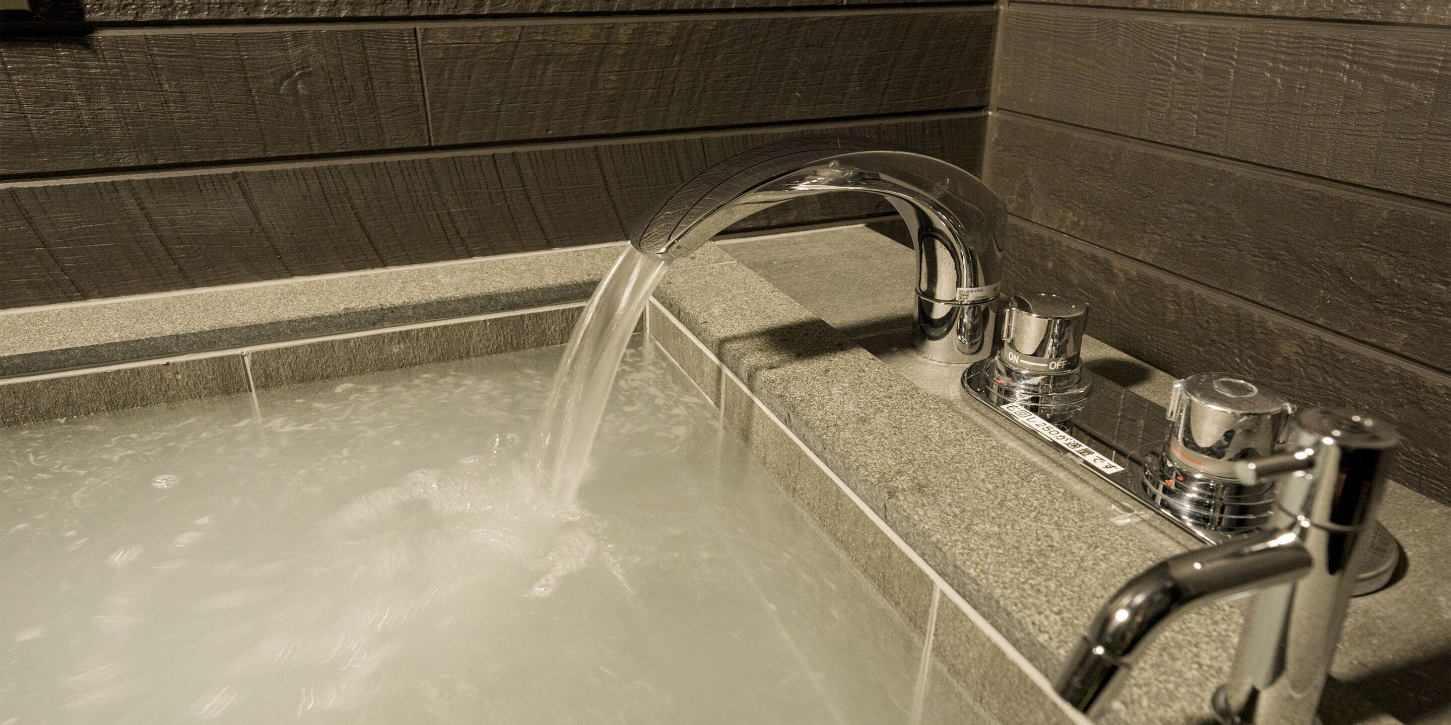 A bathtub with running water, a faucet, and a control knob.
