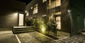 A modern building with a dark facade, multiple windows, and a small outdoor area with steps leading to a door.