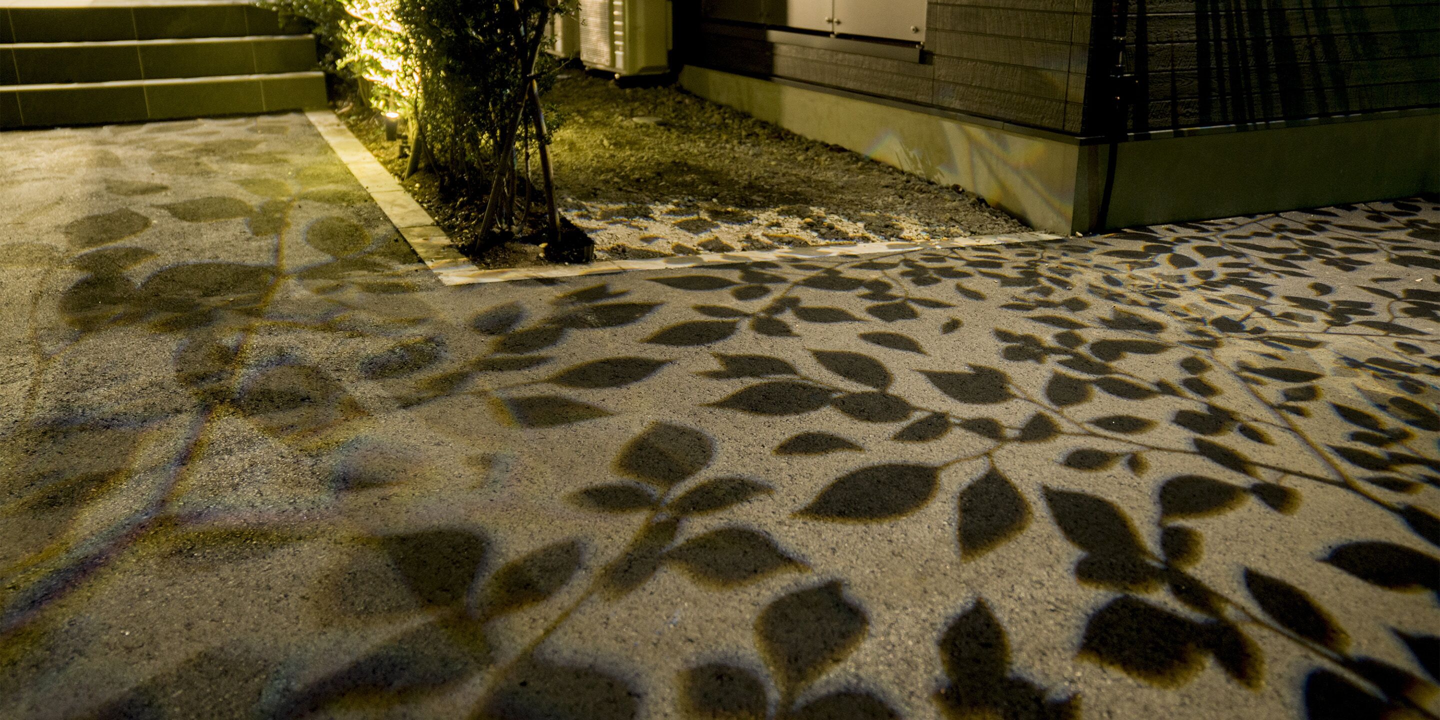 A patterned concrete patio with leaf designs, steps leading up to a building, and a small plant near the steps.