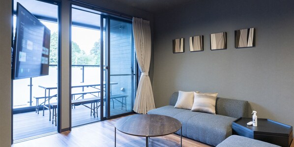 A modern living room with a grey sofa, a round coffee table, and a flat-screen TV mounted on the wall.