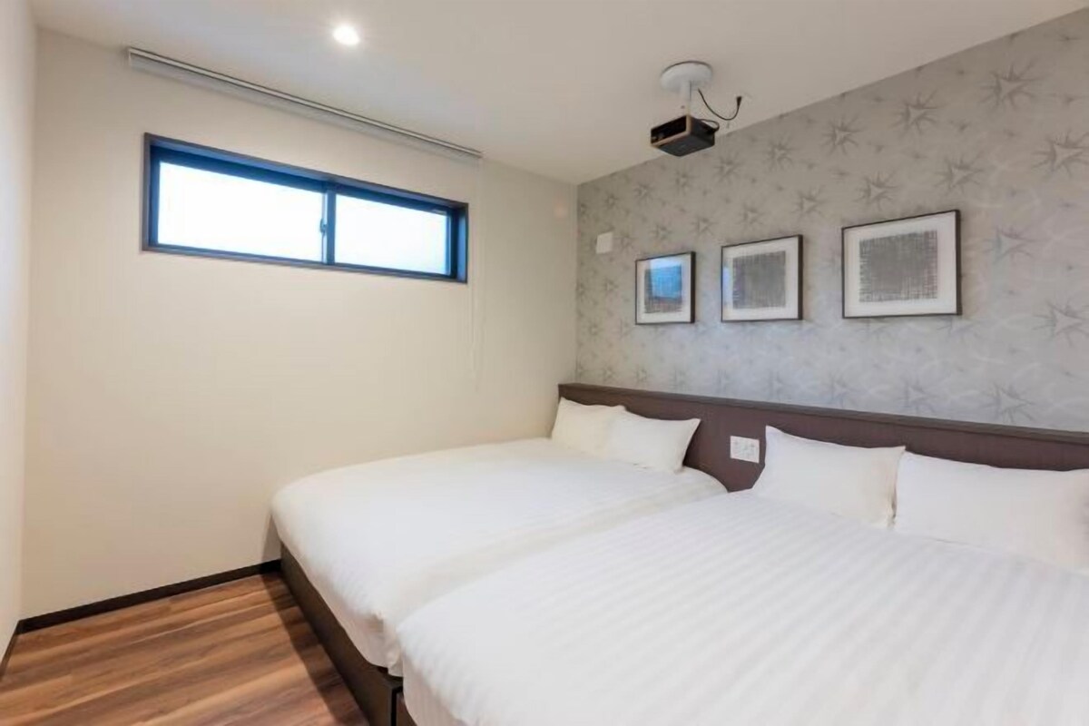 A hotel room with two beds, a window, and three framed pictures on the wall.