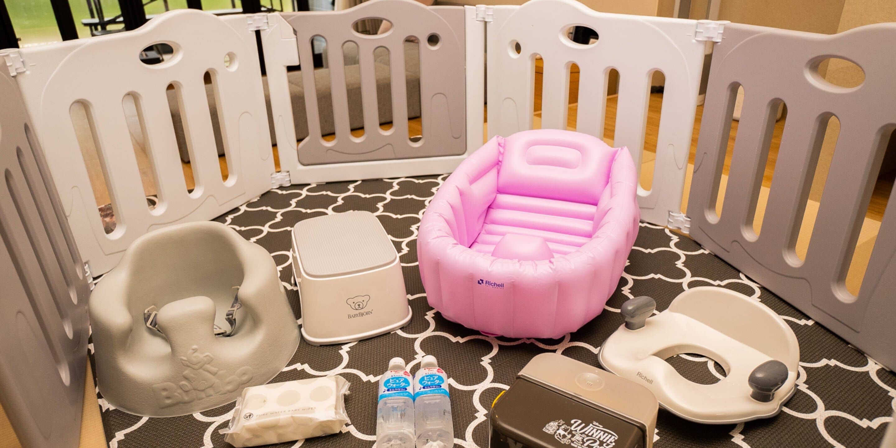 A baby play area with a pink inflatable seat, a white baby bouncer, a white changing table, a white baby bathtub, and a white baby walker.