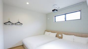 A hotel room with two beds, a ceiling projector, a window, and a wall-mounted air conditioner.