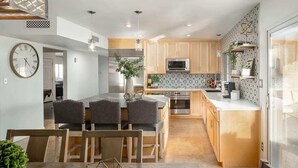 A modern kitchen with wooden cabinets, a central island, and a dining area with a table and chairs.