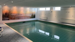 Ein Schwimmbecken mit gefliestem Boden und Wänden, einem Wandbild mit Strandmotiv und einem Fenster für natürliches Licht.